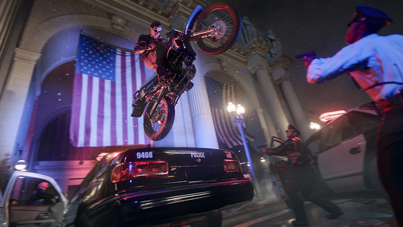 A person wearing a mask on a dirt bike ramps a police car and flies above police officers.